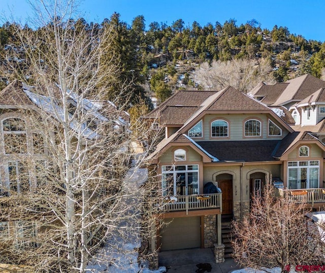 view of front of house with an attached garage, stone siding, a shingled roof, and stairway