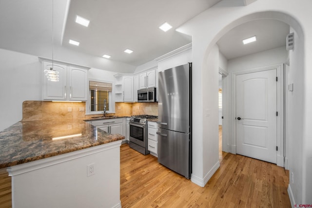 kitchen featuring stainless steel appliances, a peninsula, a sink, white cabinets, and open shelves