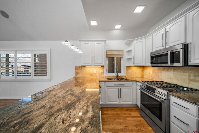 kitchen featuring stainless steel appliances, a sink, light wood-style floors, white cabinets, and backsplash