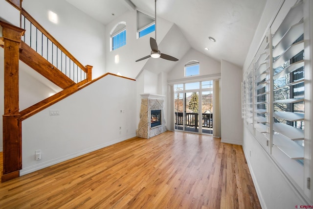 unfurnished living room featuring a tiled fireplace, ceiling fan, wood finished floors, high vaulted ceiling, and baseboards