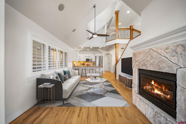 living area featuring arched walkways, high vaulted ceiling, a fireplace, baseboards, and light wood-type flooring