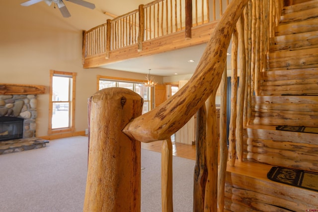 stairway featuring a towering ceiling, a fireplace, carpet flooring, and ceiling fan with notable chandelier