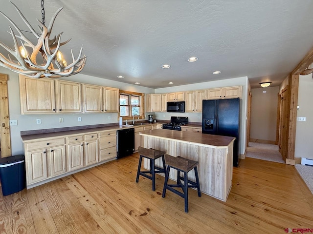 kitchen featuring light wood finished floors, dark countertops, light brown cabinetry, black appliances, and a sink