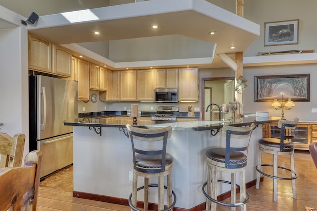 kitchen featuring stainless steel appliances, dark countertops, recessed lighting, light wood-style flooring, and a kitchen breakfast bar