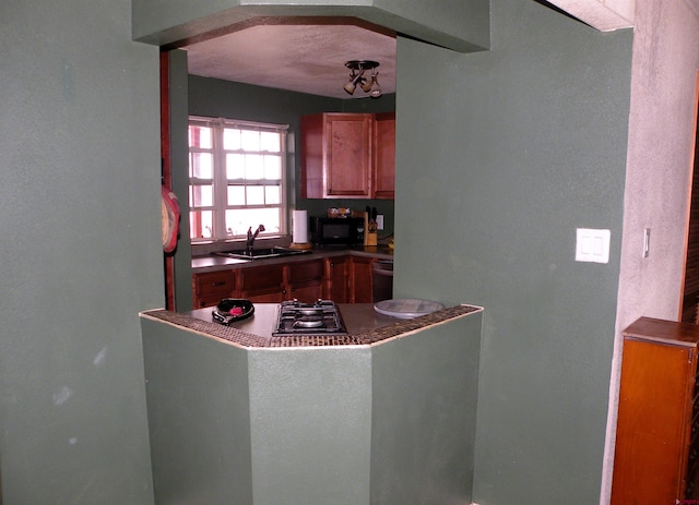 kitchen with dark countertops, brown cabinetry, black microwave, arched walkways, and a sink