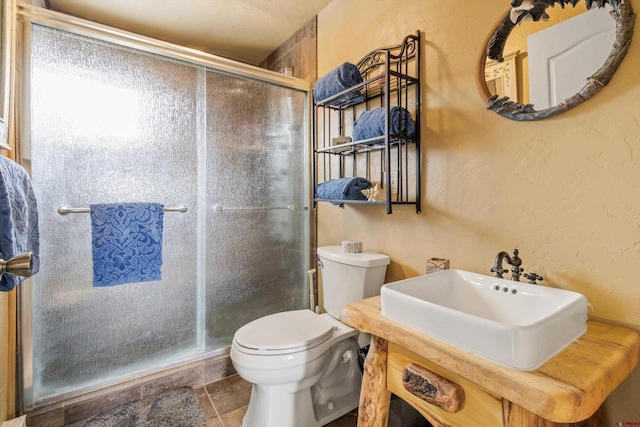 bathroom featuring toilet, a stall shower, a sink, and a textured wall