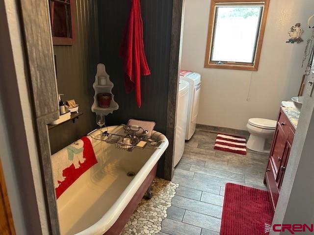 full bathroom with a freestanding tub, washing machine and dryer, toilet, vanity, and baseboards