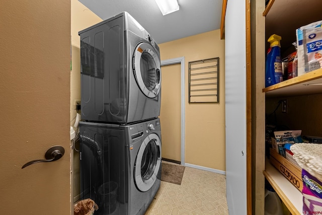 clothes washing area featuring light floors, stacked washer / drying machine, laundry area, and baseboards