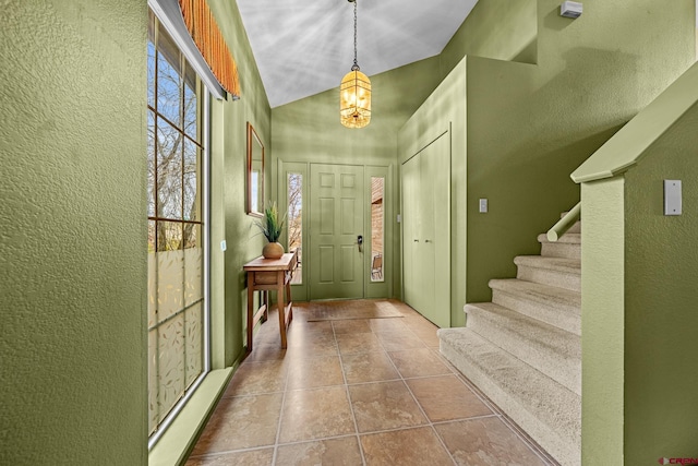 entryway with a textured wall, stairs, vaulted ceiling, and tile patterned floors