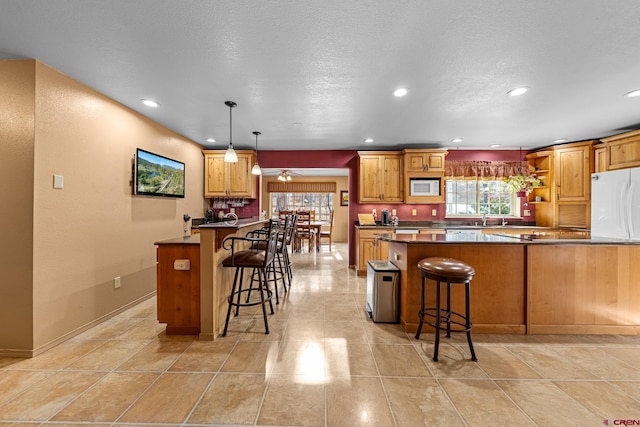 kitchen with a peninsula, white appliances, dark countertops, and a kitchen breakfast bar