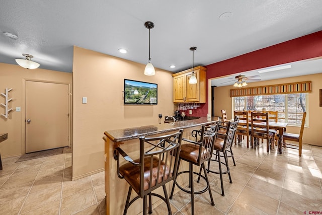 kitchen featuring light tile patterned floors, baseboards, a kitchen breakfast bar, dark stone counters, and decorative light fixtures