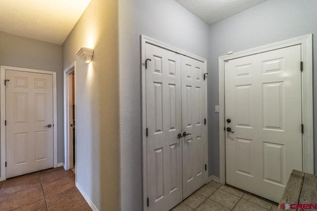 entryway featuring light tile patterned floors, a textured ceiling, and baseboards