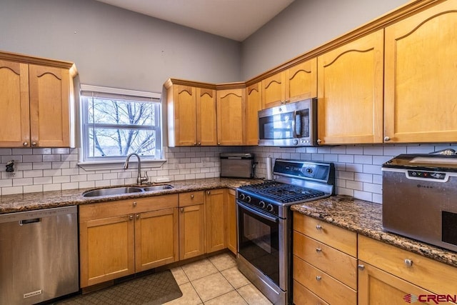 kitchen featuring light tile patterned floors, a sink, appliances with stainless steel finishes, backsplash, and dark stone counters