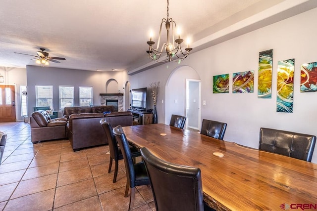 dining space featuring arched walkways, ceiling fan with notable chandelier, a fireplace, and tile patterned flooring