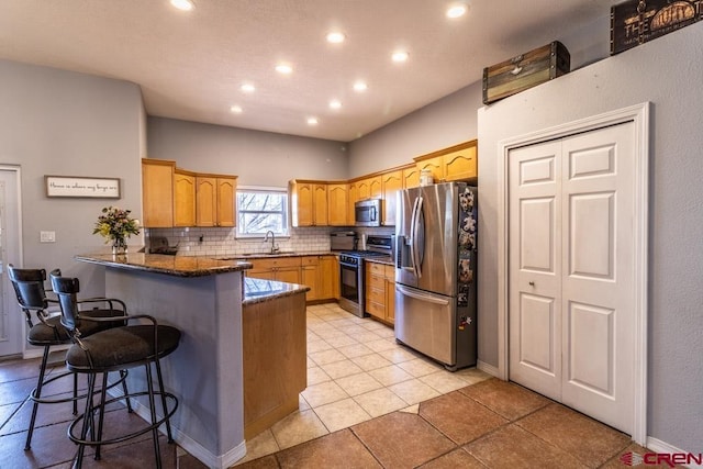 kitchen featuring a breakfast bar area, backsplash, appliances with stainless steel finishes, a sink, and a peninsula