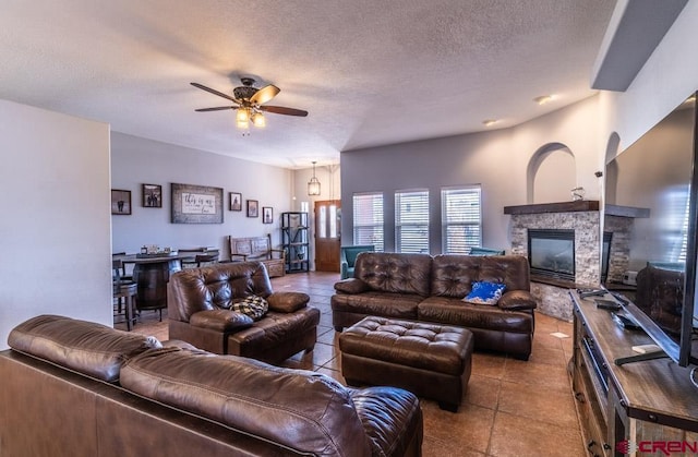 tiled living area with ceiling fan, a fireplace, and a textured ceiling