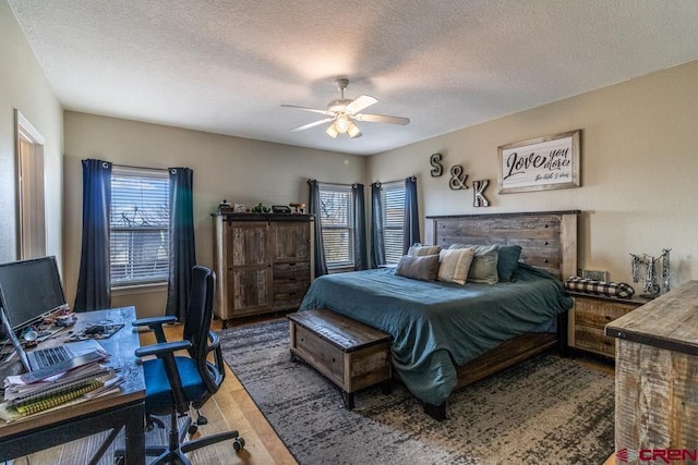 bedroom featuring a ceiling fan, multiple windows, a textured ceiling, and wood finished floors