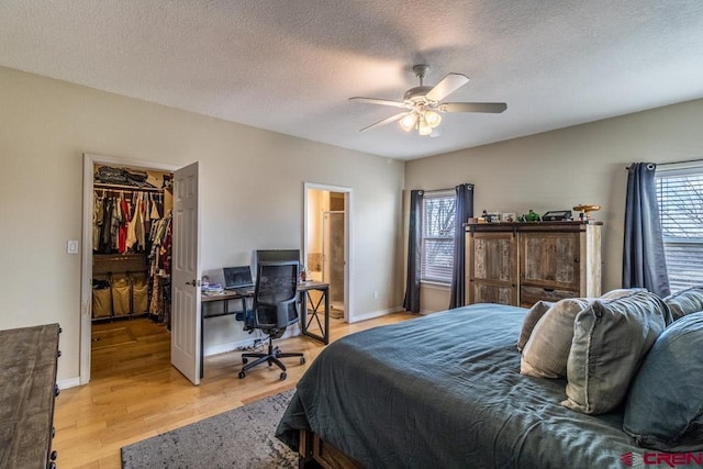 bedroom featuring a walk in closet, light wood-style flooring, a ceiling fan, a textured ceiling, and baseboards