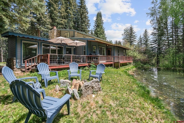 rear view of property featuring a chimney, a fire pit, and a deck with water view