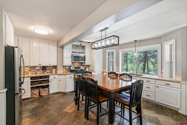 kitchen featuring stone tile floors, appliances with stainless steel finishes, decorative light fixtures, white cabinetry, and backsplash