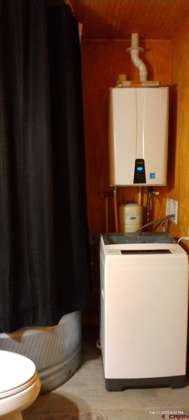 bathroom with tankless water heater, toilet, wood walls, wood ceiling, and washer / dryer