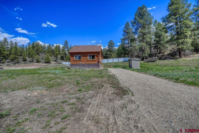 view of front of house featuring driveway, fence, and log siding