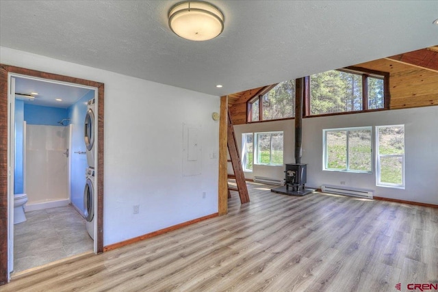 spare room featuring a baseboard heating unit, light wood finished floors, stacked washer / dryer, and a wood stove