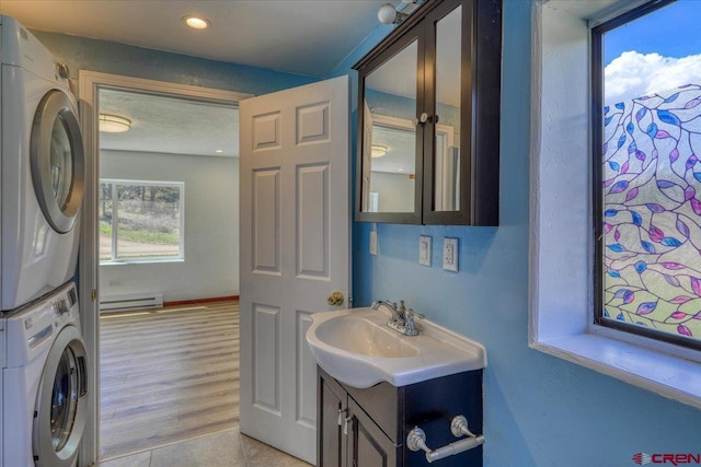 laundry room featuring stacked washer and dryer, laundry area, light wood finished floors, a baseboard heating unit, and a sink