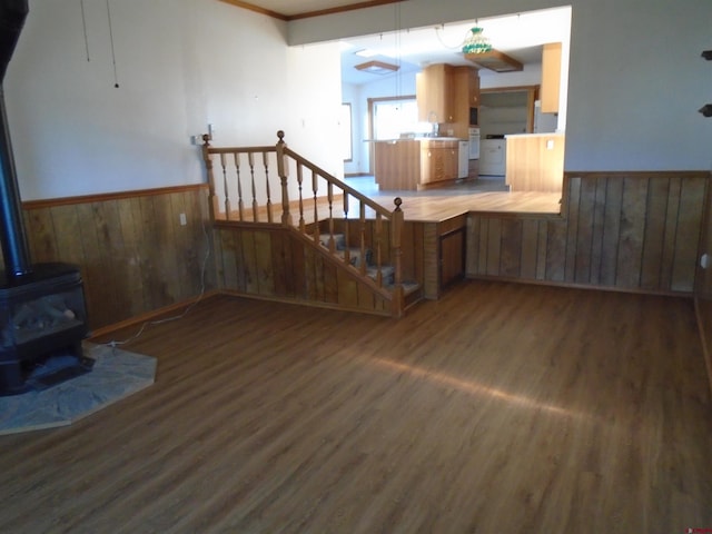 unfurnished living room featuring a wainscoted wall, stairs, wood finished floors, and a wood stove