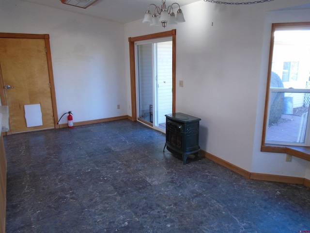 spare room featuring a wood stove, baseboards, and a notable chandelier