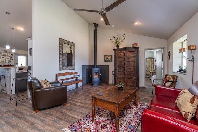 living room with ceiling fan, a wood stove, vaulted ceiling, and wood finished floors