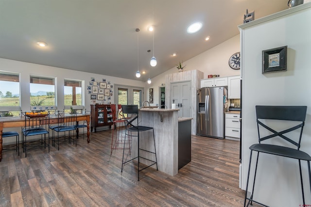 kitchen featuring a breakfast bar, decorative light fixtures, stainless steel refrigerator with ice dispenser, dark wood-type flooring, and white cabinets