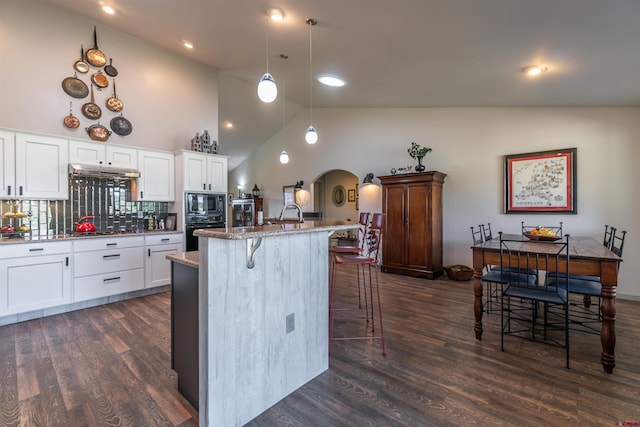 kitchen featuring black appliances, a kitchen bar, arched walkways, and dark wood-style floors