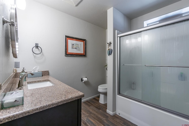 full bathroom featuring toilet, wood finished floors, vanity, baseboards, and combined bath / shower with glass door