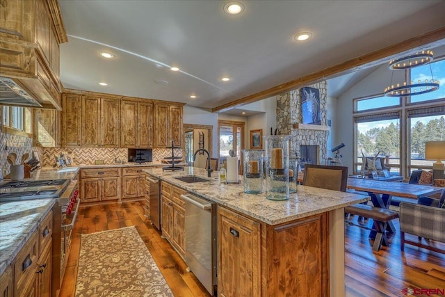 kitchen with appliances with stainless steel finishes, brown cabinetry, a healthy amount of sunlight, vaulted ceiling, and a sink