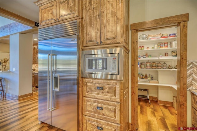 kitchen featuring built in appliances, light wood finished floors, and baseboards