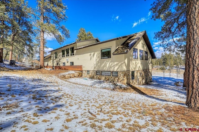 view of snow covered exterior featuring stone siding and stucco siding