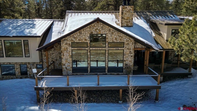 snow covered rear of property featuring a standing seam roof, a chimney, metal roof, and stucco siding