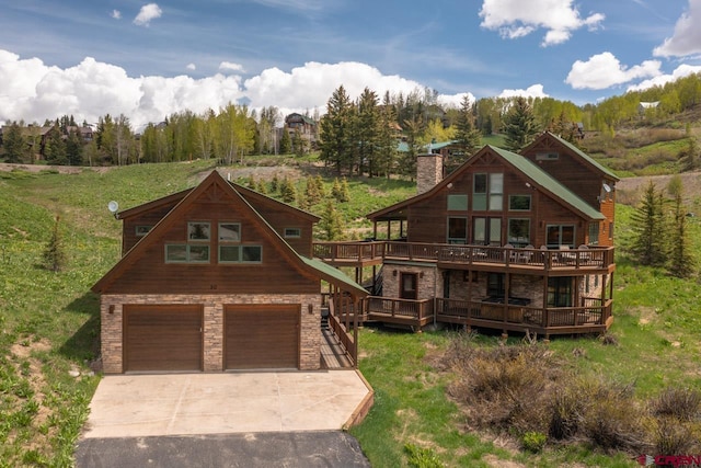 view of front of property featuring a chimney, an attached garage, a deck, stone siding, and driveway