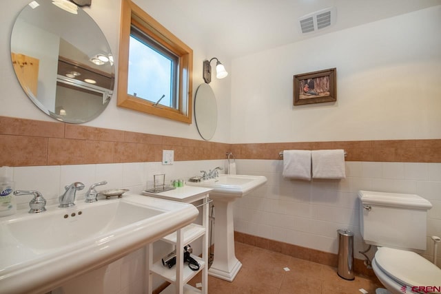 bathroom with tile walls, visible vents, toilet, a sink, and tile patterned flooring