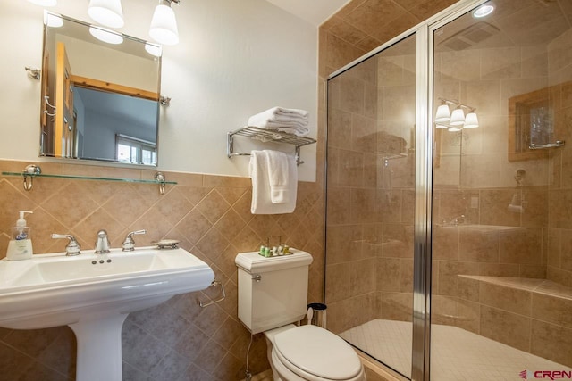 full bathroom with toilet, a shower stall, tile walls, and a sink