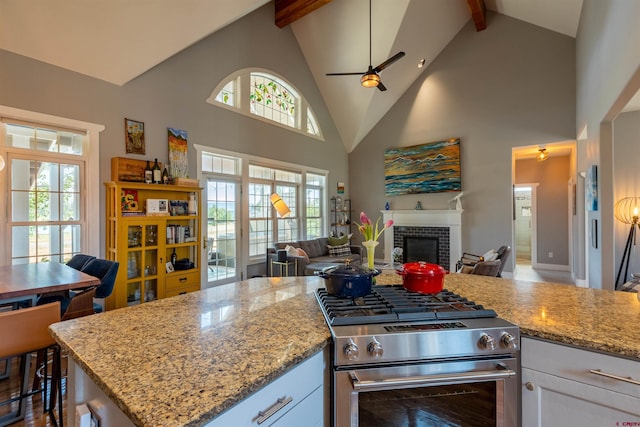 kitchen with open floor plan, stainless steel range, a fireplace, and white cabinets