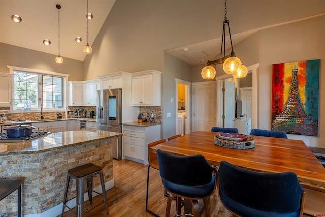 kitchen featuring light wood finished floors, light stone countertops, stainless steel appliances, white cabinetry, and backsplash