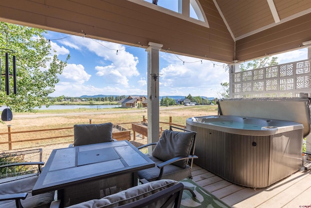 wooden terrace featuring a water view, a hot tub, and outdoor dining area