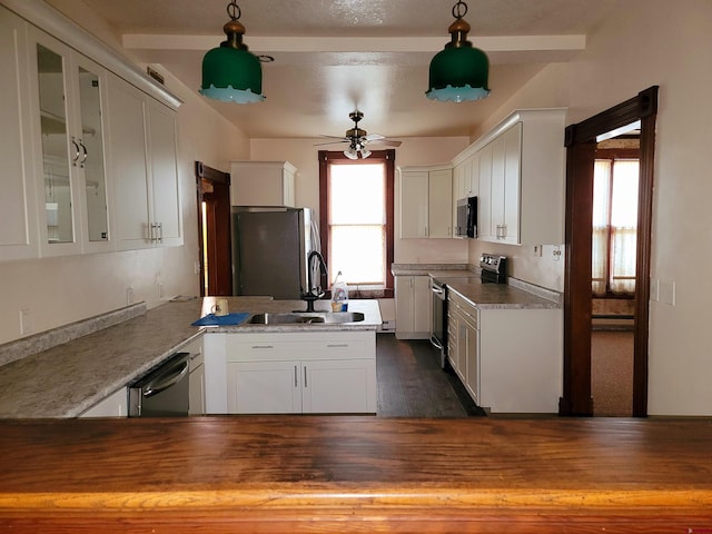 kitchen with appliances with stainless steel finishes, glass insert cabinets, white cabinets, a sink, and a peninsula