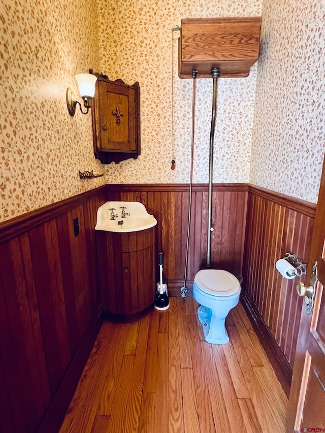 bathroom with toilet, wainscoting, wooden walls, wood finished floors, and wallpapered walls