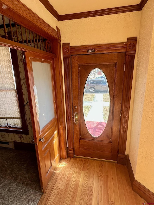 entryway featuring ornamental molding, baseboard heating, light wood-style floors, and baseboards