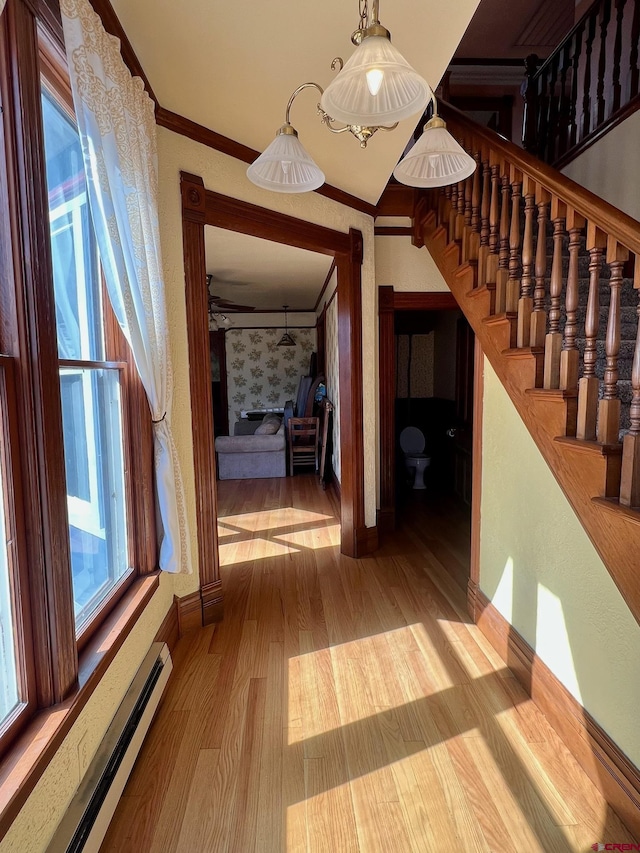 interior space featuring stairway, a baseboard heating unit, ornamental molding, wood finished floors, and baseboards