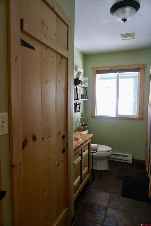 bathroom featuring stone tile flooring, toilet, vanity, and baseboard heating