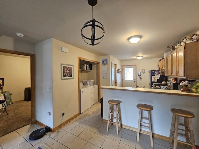 kitchen with a breakfast bar, washer and clothes dryer, light tile patterned floors, a peninsula, and baseboards